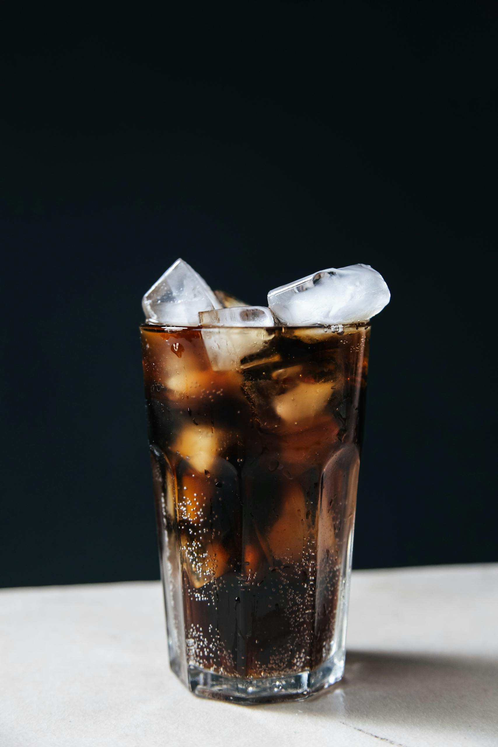 Refreshing glass of cola with ice cubes against a dark background, perfect for summer.